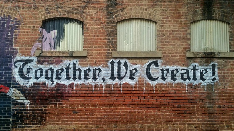 The words Together We Create painted on a brick wall